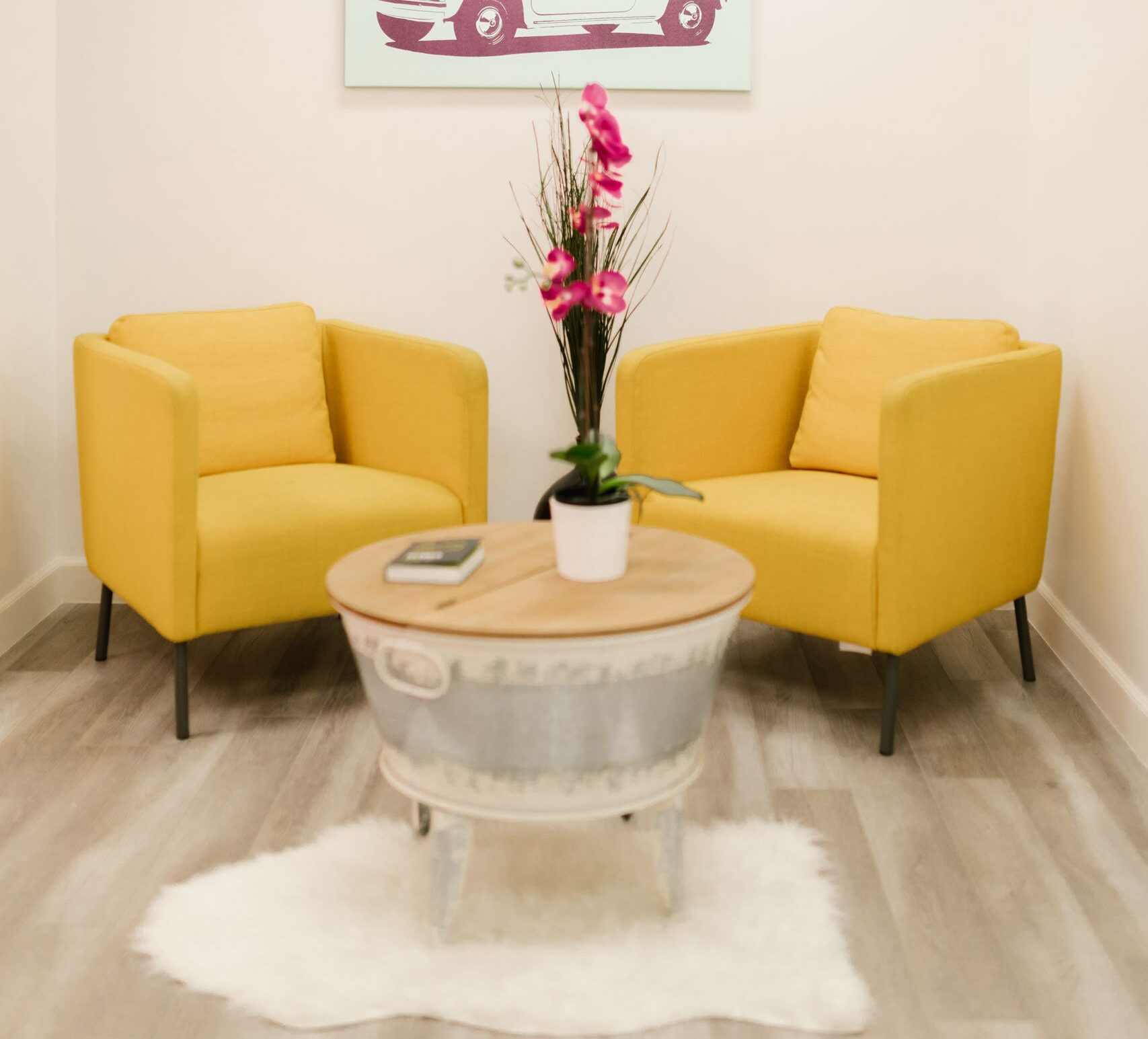 Bright waiting area featuring yellow chairs, a modern table, and car artwork.